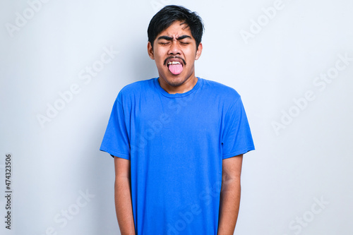 Boy wearing casual shirt sticking tongue out happy with funny expression. Emotion concept.