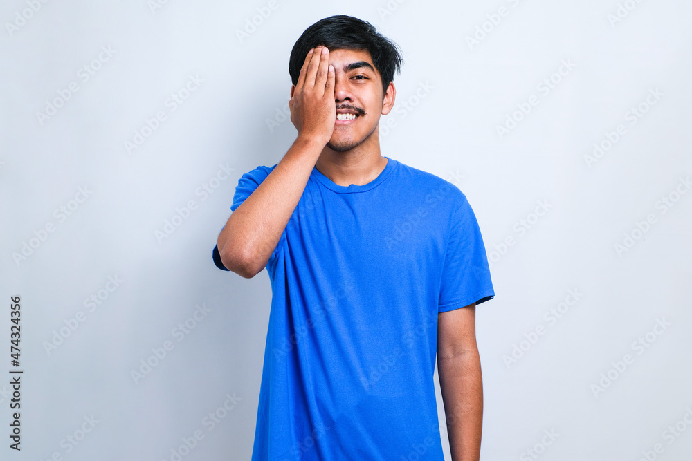 Asian man wearing casual shirt covering one eye with hand Asian man wearing casual shirt covering one eye with hand