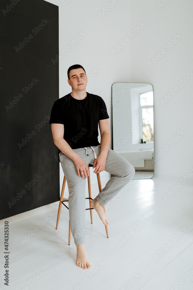 Smart young man seated on chair, posing while looking at camera in studio background