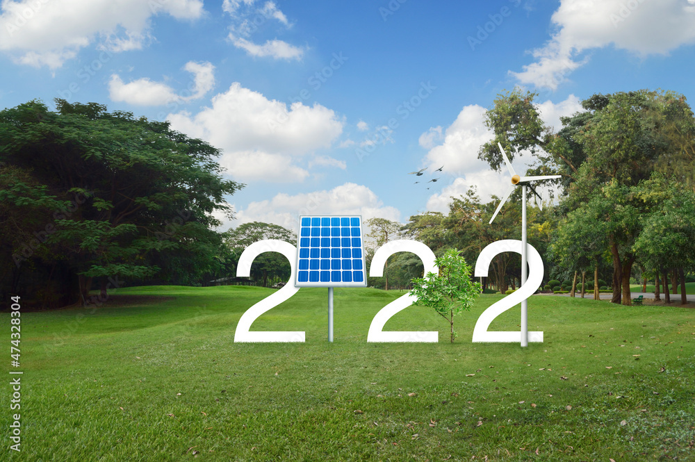 Fototapeta premium 2022 white text with solar cell, wind turbine and growing tree on green grass field in public park, Happy new year 2022 ecological cover concept