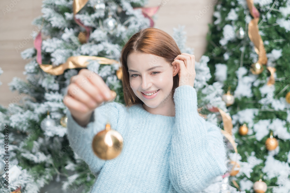 New Year portrait of beautiful caucasian young woman in cozy wool warm light blue sweater holding a gold ball for decoration christmas tree.
