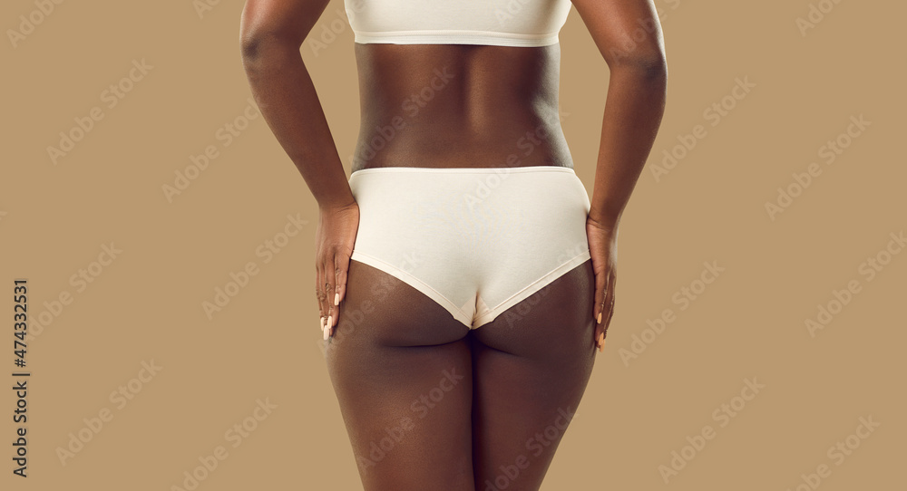 Closeup back view plus size black female model in underwear. Close up backview attractive young African woman wearing white natural cotton underpants standing isolated on solid beige color background