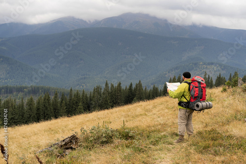 bearded Caucasian male tourist on stands with a map on a mountain trail while hiking in the mountains. © mtrlin