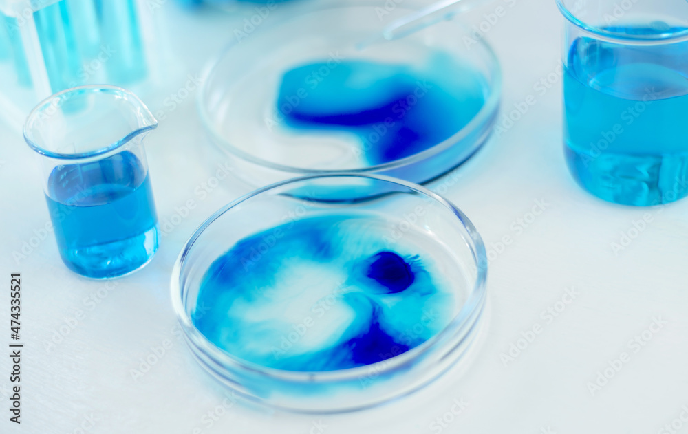 Laboratory glassware with blue and cyan liquid on a white table. Scientific laboratory research. Antiviral vaccine development. Laboratory glassware with blue and cyan liquid on a white table. Scientific laboratory research. Antiviral vaccine development.