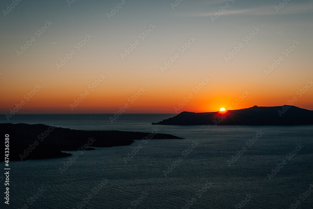 The sun sets behind an island in the sea, Santorini, Greece