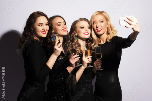 Celebration, party, and people concept - four fashionable young women drinking champagne and taking a selfie