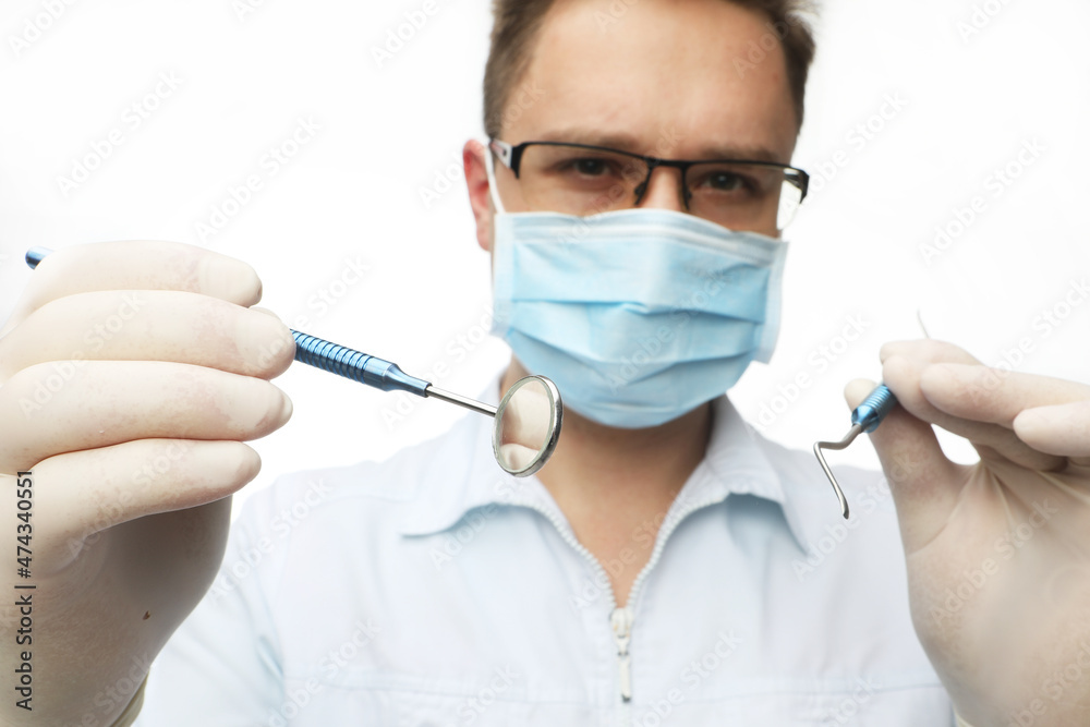 Young dentist male in white lab coat and mask holding dental instruments Young dentist male in white lab coat and mask holding dental instruments