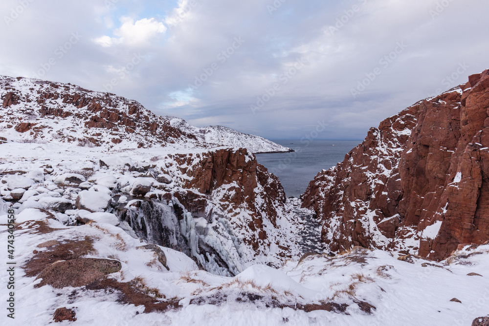 Brown rocks in the snow, view of the northern ocean. Teriberka village, Murmansk region, Russia.