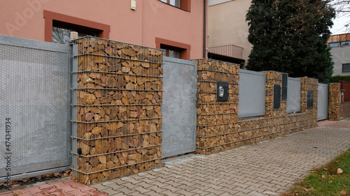 Gabion retaining wall - brown stones in gabion metallic baskets kept by retaining wall. Modern privacy fence of natural stones and galvanized steel grid surrounding residential House.  photo