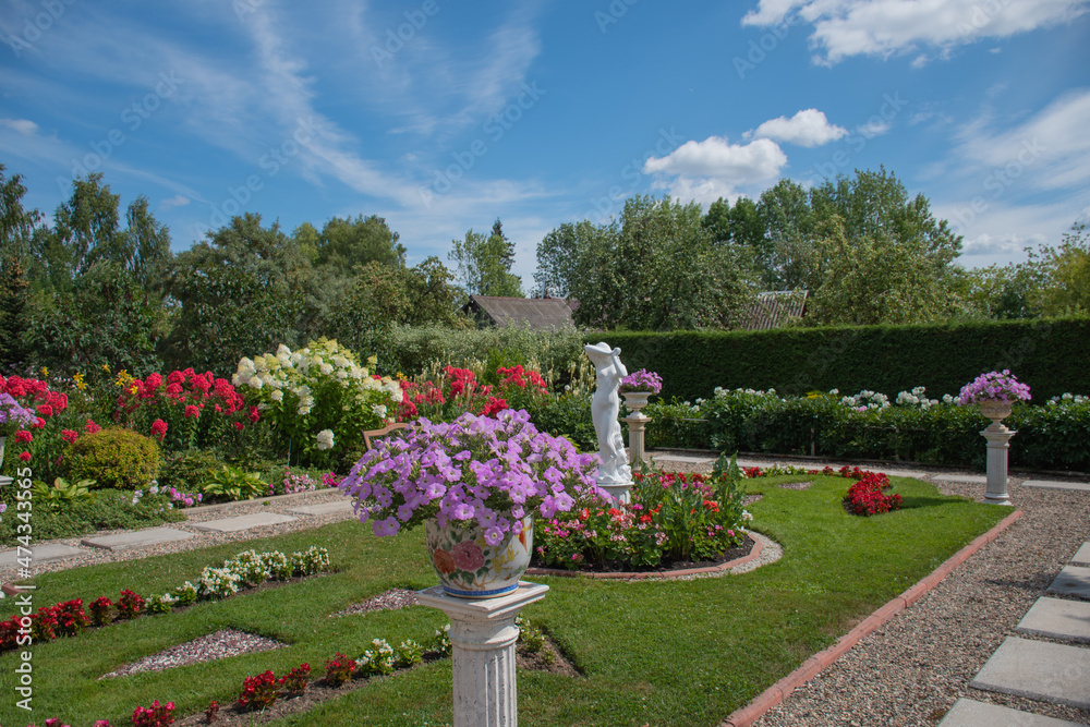 Landscaping of the garden plot: a hot summer day, a flower courtyard of hydrangeas, phlox and a garden statue with bright colors in vases and on the lawn, selective focus on petunias