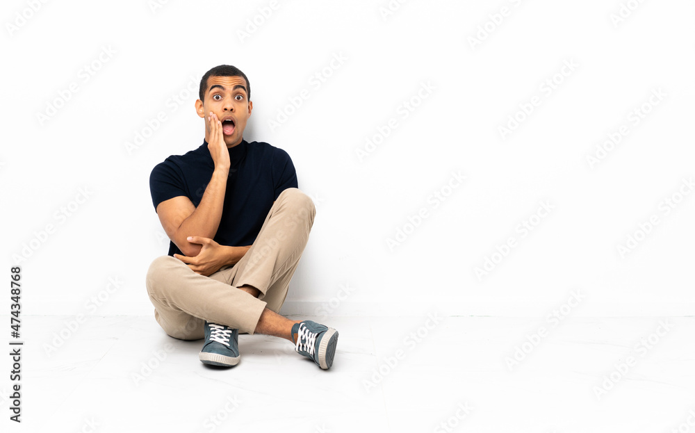 African American man sitting on the floor surprised and shocked while looking right African American man sitting on the floor surprised and shocked while looking right