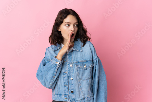 Teenager Ukrainian girl isolated on pink background whispering something with surprise gesture while looking to the side