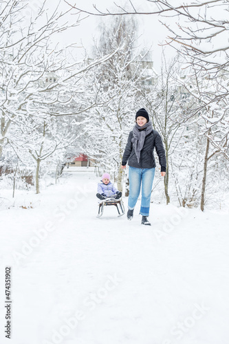 Mom is rolling a small child on a sled in the snow.