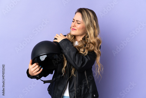 Young Brazilian woman holding a motorcycle helmet isolated on purple background suffering from pain in shoulder for having made an effort