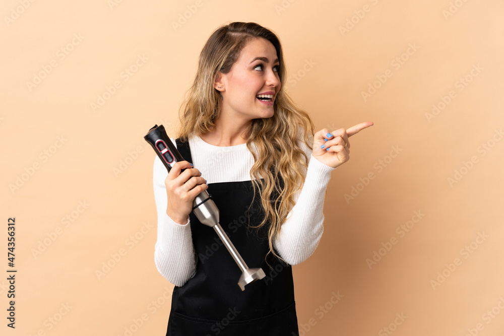 Young brazilian woman using hand blender isolated on beige background intending to realizes the solution while lifting a finger up Young brazilian woman using hand blender isolated on beige background intending to realizes the solution while lifting a finger up