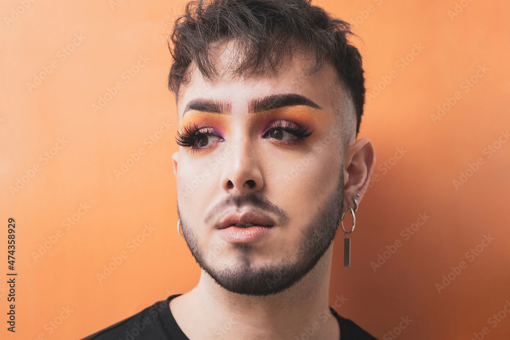 The portrait of a guy gay with makeup on an orange background.diversity concept. The portrait of a guy gay with makeup on an orange background.diversity concept.