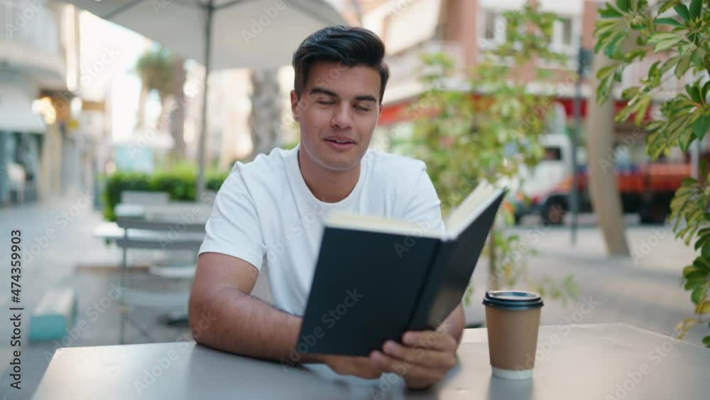 Young hispanic man smiling confident reading book at coffee shop terrace Young hispanic man smiling confident reading book at coffee shop terrace
