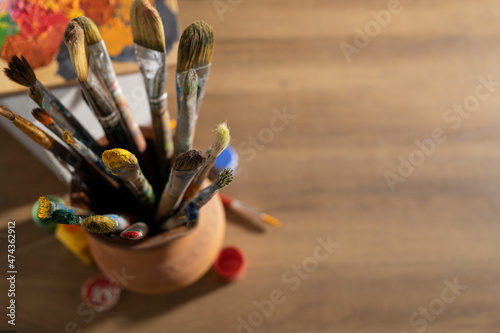 Artist supplies on wooden table. Paint brush in clay jug and art painter tools on wood desk