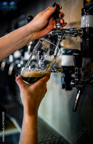 woman bartender hand at beer tap pouring a dark beer in glass serving in a restaurant or pub