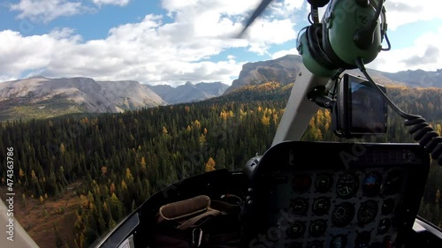 Inside of pilot flying a helicopter on autumn forest in rocky mountains