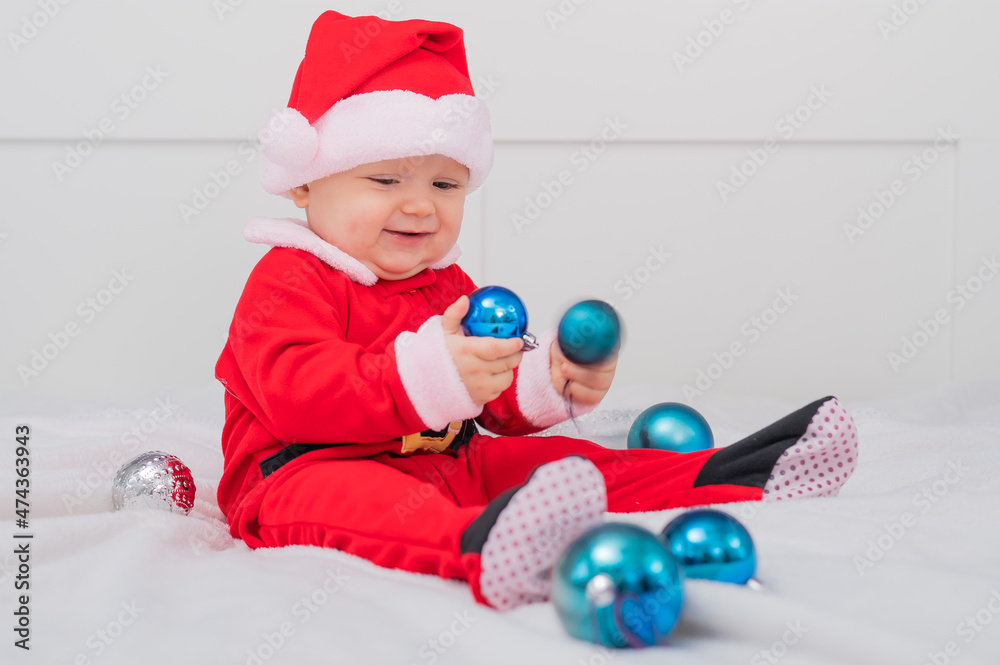 Baby boy dressed as Santa is playing with Christmas decorations on the bed. Baby boy dressed as Santa is playing with Christmas decorations on the bed.