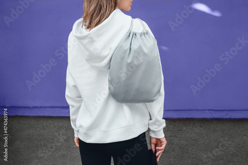 Grey drawstring pack template, mockup of bag for sport shoes on woman's shoulder standing on a violet or very peri background. photo
