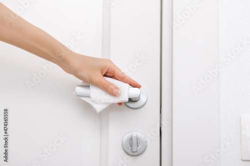 Cleaning door handles with an antiseptic wet wipe and gloves. Sanitize surfaces prevention in hospital and public spaces against corona virus. Woman hand using towel for cleaning home room door link.