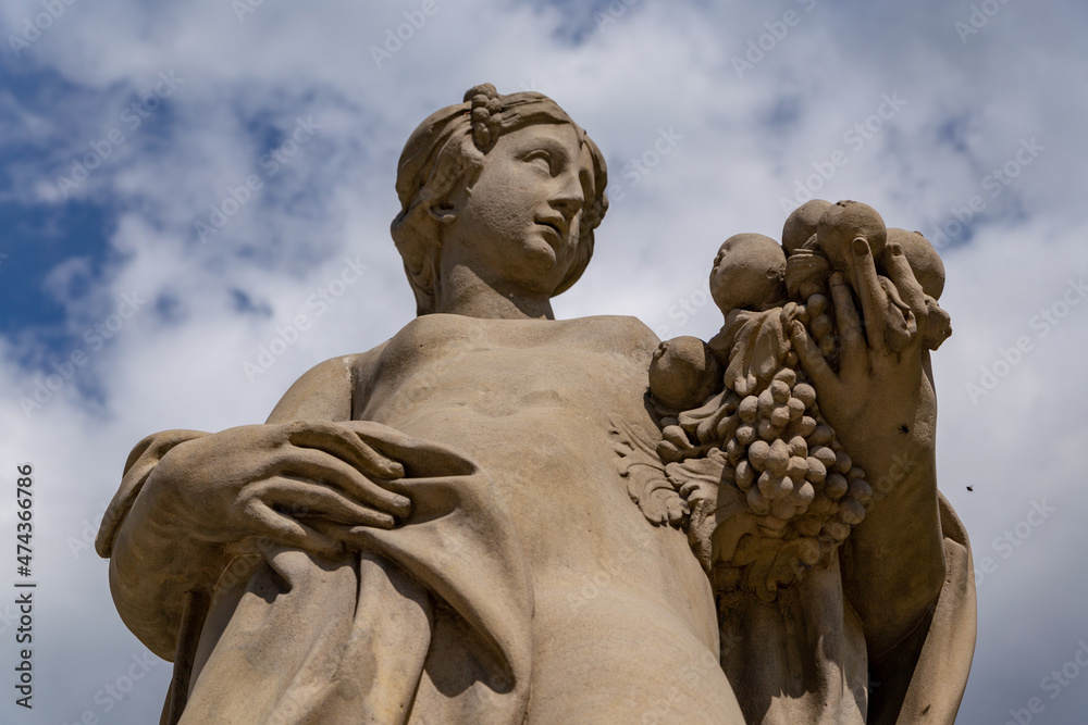 antique statue of a woman with grapes in her hand on a background of sky in the royal garden of Wilanow Palace Warsaw Poland