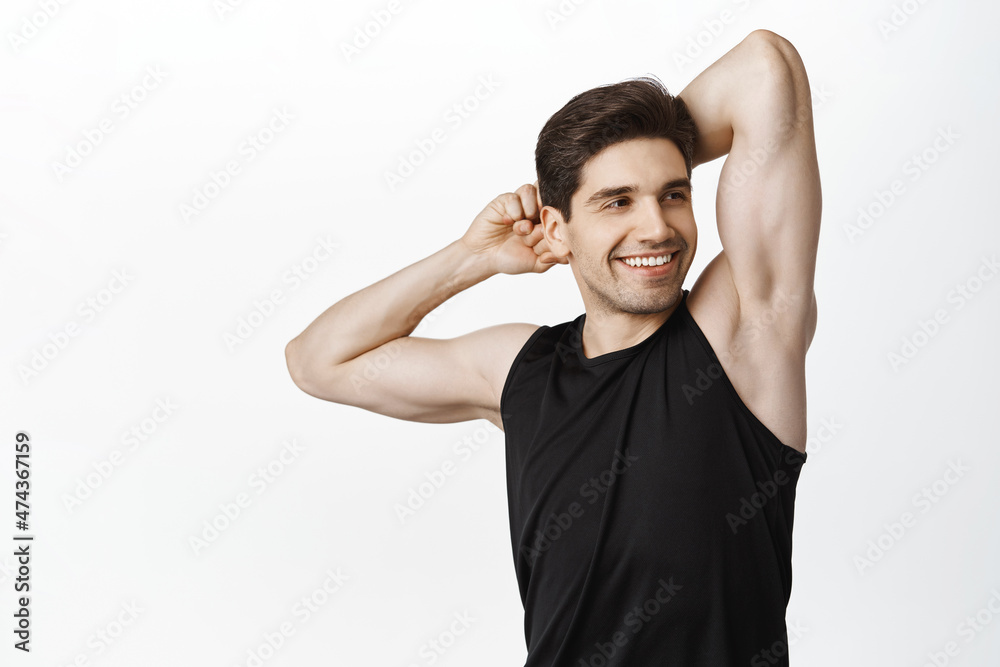 Strong and handsome man with biceps, masculine body, stretching arms and smiling, warm up in gym, workout process, white background Strong and handsome man with biceps, masculine body, stretching arms and smiling, warm up in gym, workout process, white background