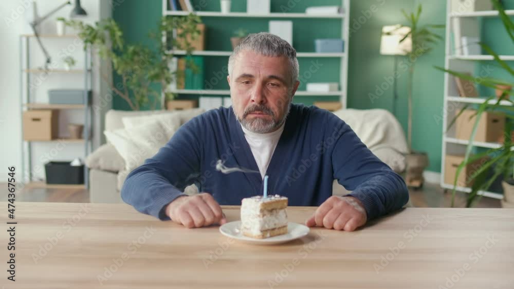 A Sad Elderly Man Celebrates the Holiday Alone, Blowing out the Candle on the Cake, Feeling Parting, Disappointment, Loss. Drama, Isolation, Old Age. Nursing Home Concept, Mental Health.
