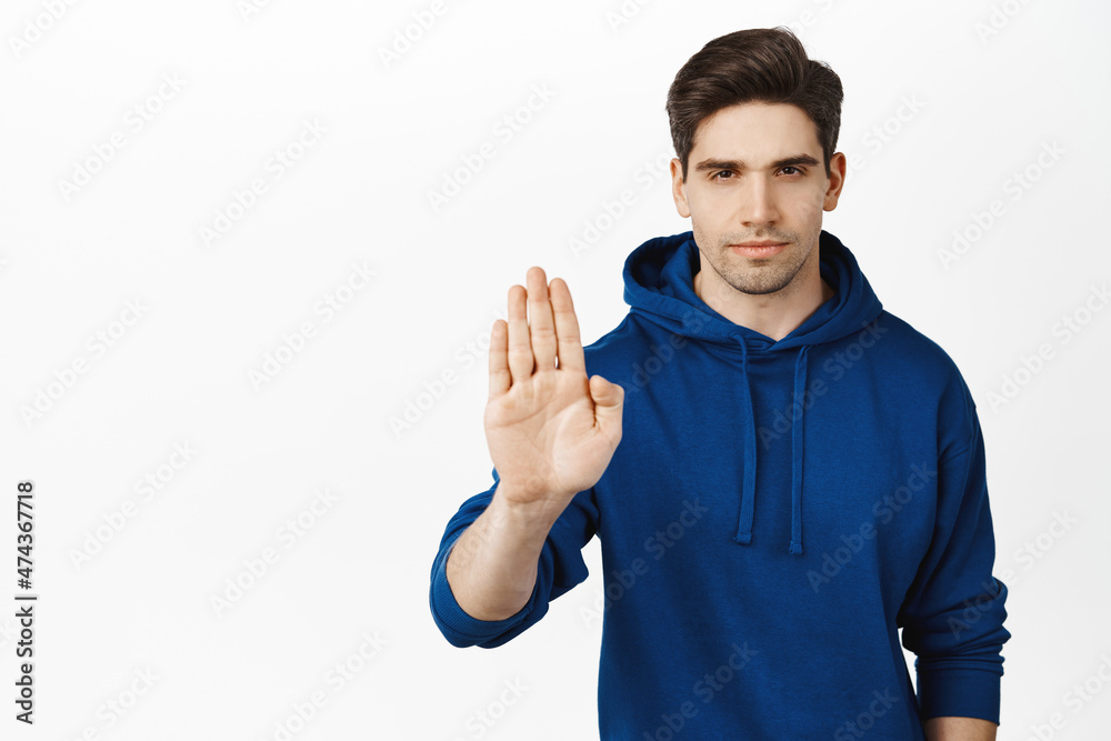 No. Serious and confident man showing stop, taboo block sign, raising palm in prohibition gesture, standing in hoodie over white background No. Serious and confident man showing stop, taboo block sign, raising palm in prohibition gesture, standing in hoodie over white background