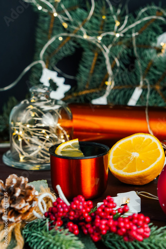 Lemon tea in orange metal mug and lemon at Christmas illuminated decoration. Selective focus