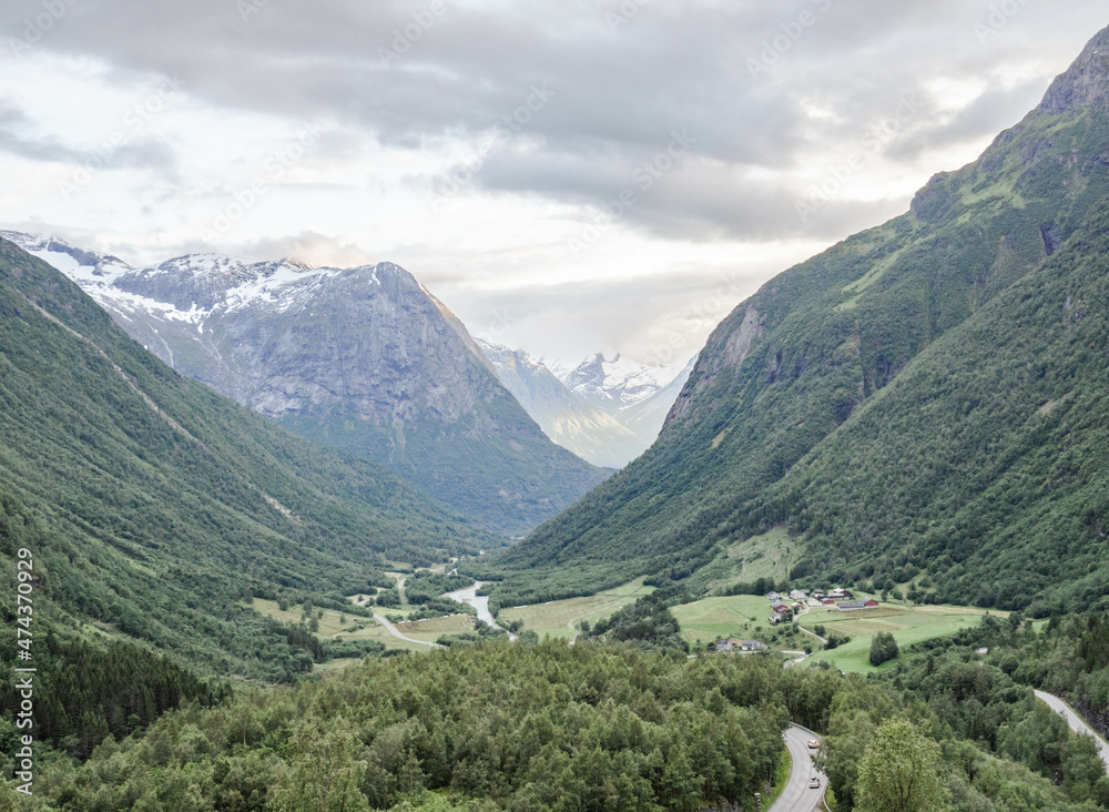 Norwegian landscape with green valley between mountains with snow peaks.