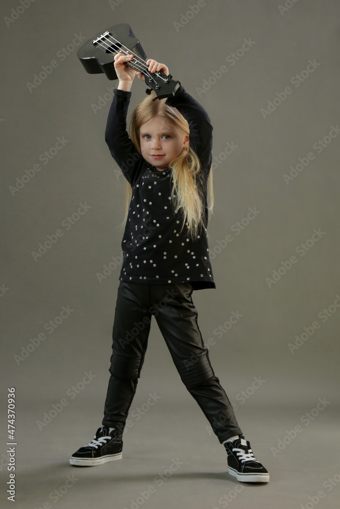 Naklejka premium Studio portrait of toddler girl guitarist breaking her guitar, studio shop on grey background.