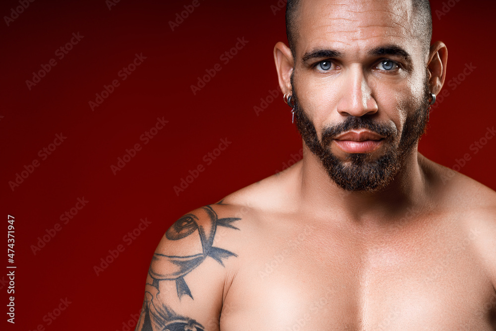 Studio portrait of beautiful blue-eyed Cuban or Latinos with muscular inflated shirtless body. Beautiful body in tattoos. Masculine strength and confidence.