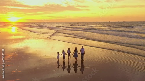 Aerial view of silhouettes of happy family walking and holding the hands each other on beach during sunset
