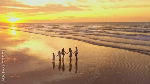 Aerial view of silhouettes of happy family walking and holding the hands each other on beach during sunset