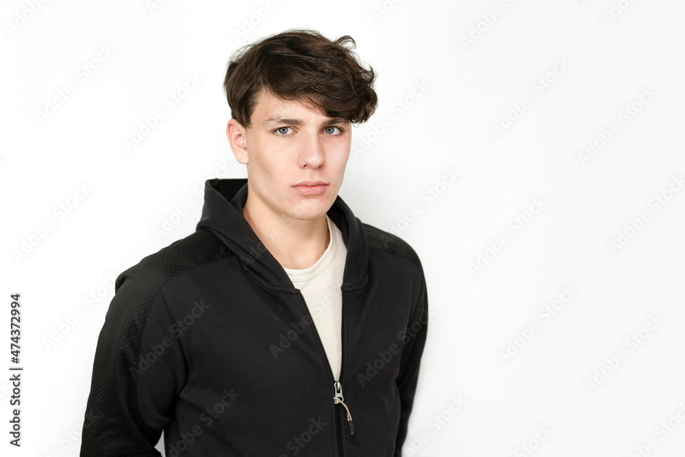 Sad teenager boy on a light background, the boy has black curly hair and a dark sports jacket. The boy is tired of studying and needs rest, he has a headache Sad teenager boy on a light background, the boy has black curly hair and a dark sports jacket. The boy is tired of studying and needs rest, he has a headache