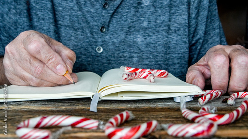 Man hands with pencil and notebook on wooden table with peppermint candy