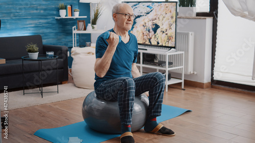Fotografie Senior man lifting dumbbells and sitting on fitness toning ball to do physical training and exercise