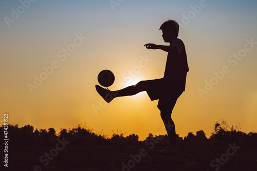 Silhouette action sport outdoor of a young man having fun playing soccer football for exercise in community rural area under the twilight sunset.