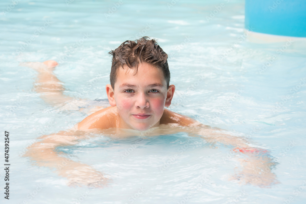 A happy boy lies in the water park in the pool.