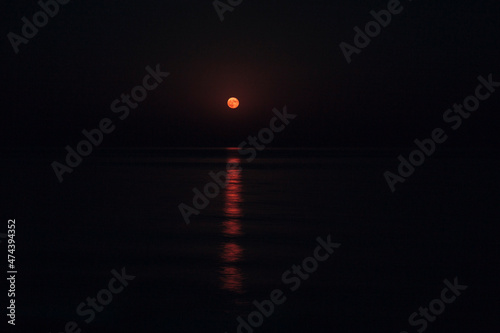 The Full Red Moon Shines Brightly in the Sky on a Dark Night Over the Calm Sea. Beautiful Moon Path on the Water photo