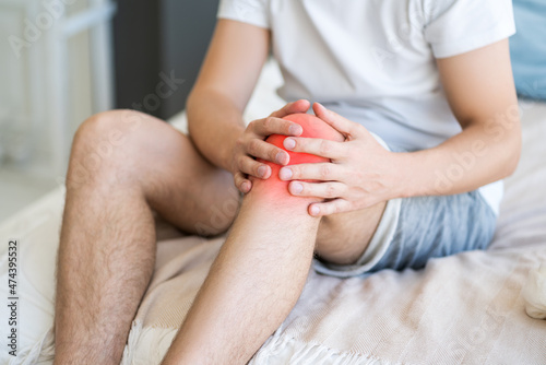 Knee pain, man suffering from ache and doing self-massage at home