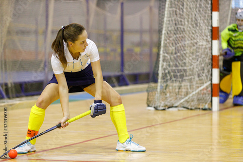 Young female player performing penalty or corner shot in indoor hockey game.
