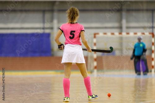 Young female indoor hockey player standing with the ball across goalkeeper.