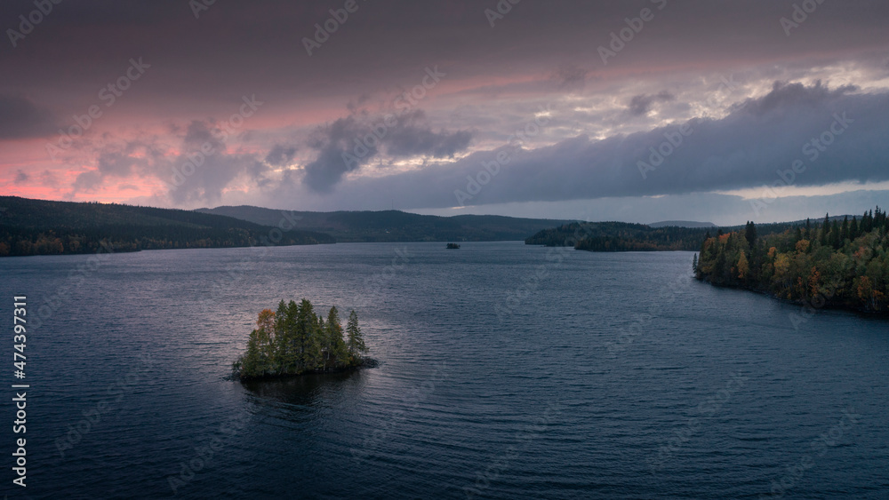 Island with trees in lake on Wilderness Road in Lapland in Northern Sweden, in the sunset from above.