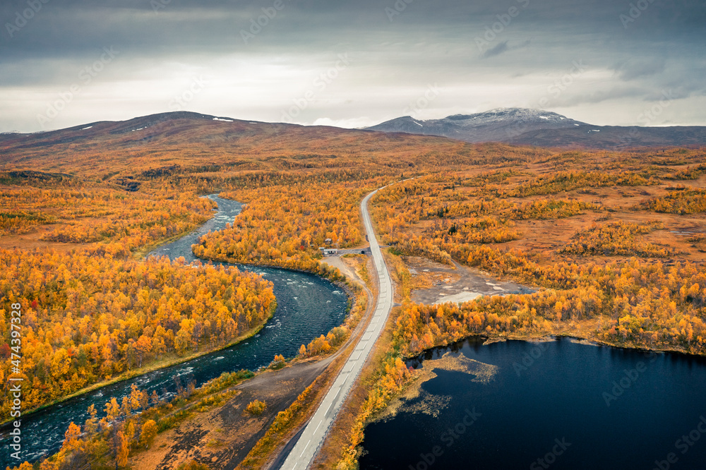 Blue lake and river, following a lonesome road to mountains with yellow trees in autumn along the scenic Wilderness Road in Lapland in Sweden from above.