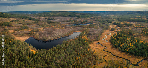 Wild landscape with forest, lake and river in autumn in Jämtland in Sweden from above, coloured trees and cloudy sky.