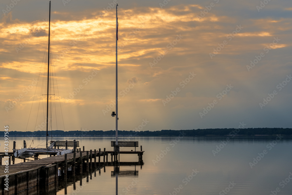 A bench on a jetty with the evening sun shining through the clouds, and a view at the Steinhuder Meer in Fluegelhorst, Lower Saxony, Germany